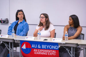 3 student panelists sit behind an AU & Beyond sign in a classroom. One student is speaking.