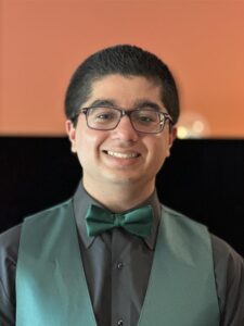 A photo of a young man with buzzed, dark hair, and glasses wearing a button up and bowtie.