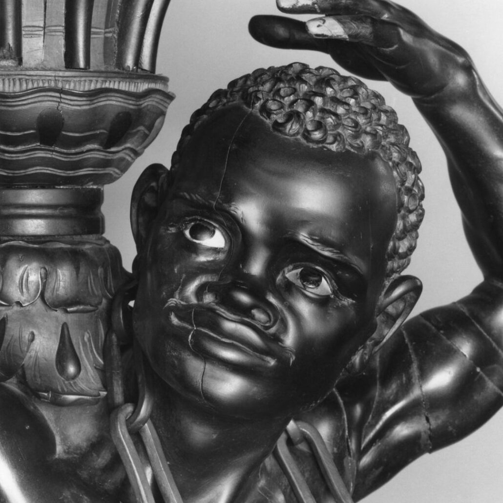 Black and white photograph of a dark-skinned male sculpture which is a vase holder