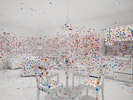 A painted white room covered sparingly with circular rainbow stickers. The room has four chairs, a table, a visible couch and kitchen area. The hanging ceiling lamp is also not fully covered with stickers.
