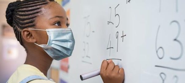 Black schoolgirl solving addition sum on white board during Covid-19 pandemic.