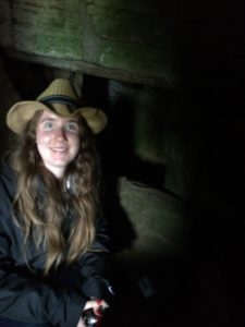 Paige Magrogan sitting in cave wearing straw Panama hat, smiling at the camera.