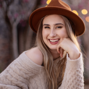 Hannah Shows, host of the Type A podcast, is smiling at the camera in a knit sweater and brown felt hat.
