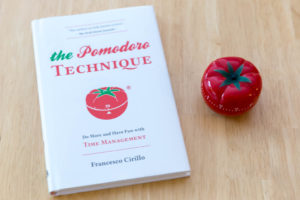 A tomato and a book rest on a table, both represent the pomodoro study technique.